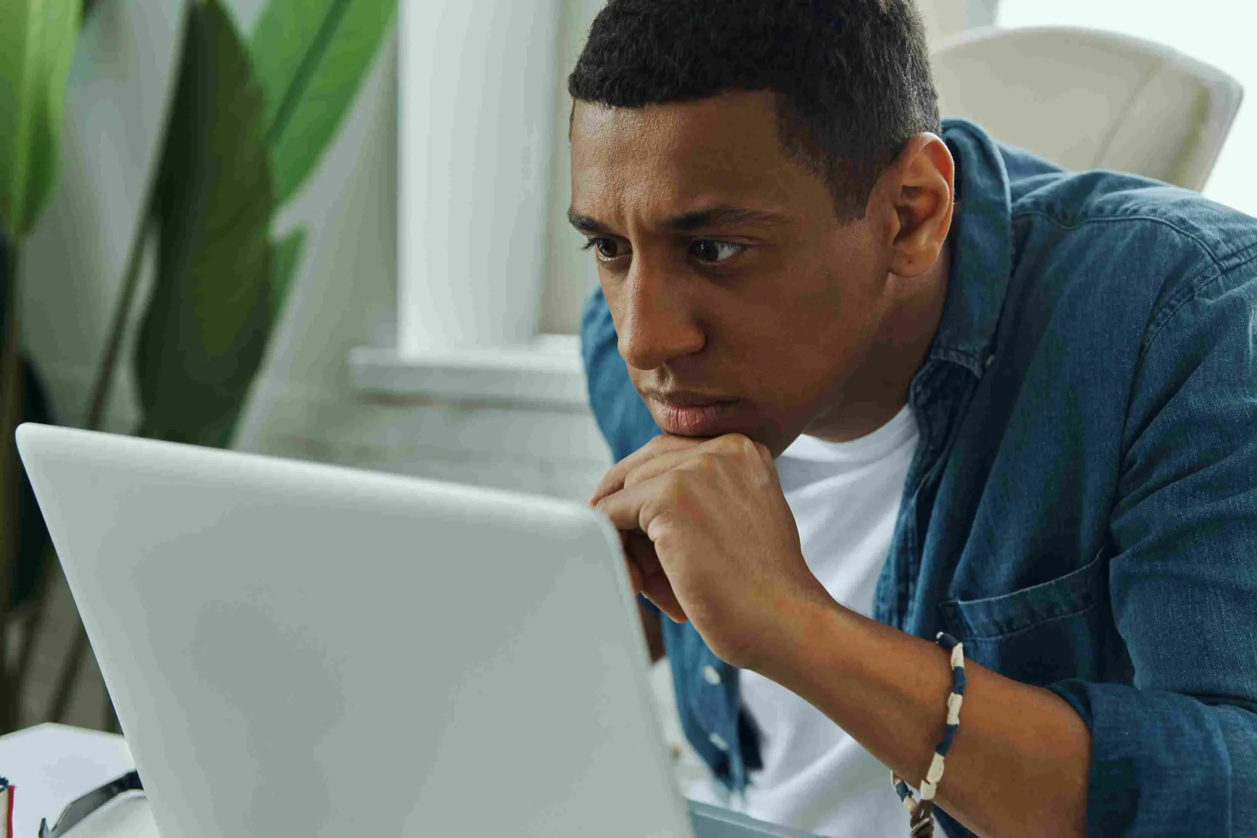 Man focused on laptop in a bright room.