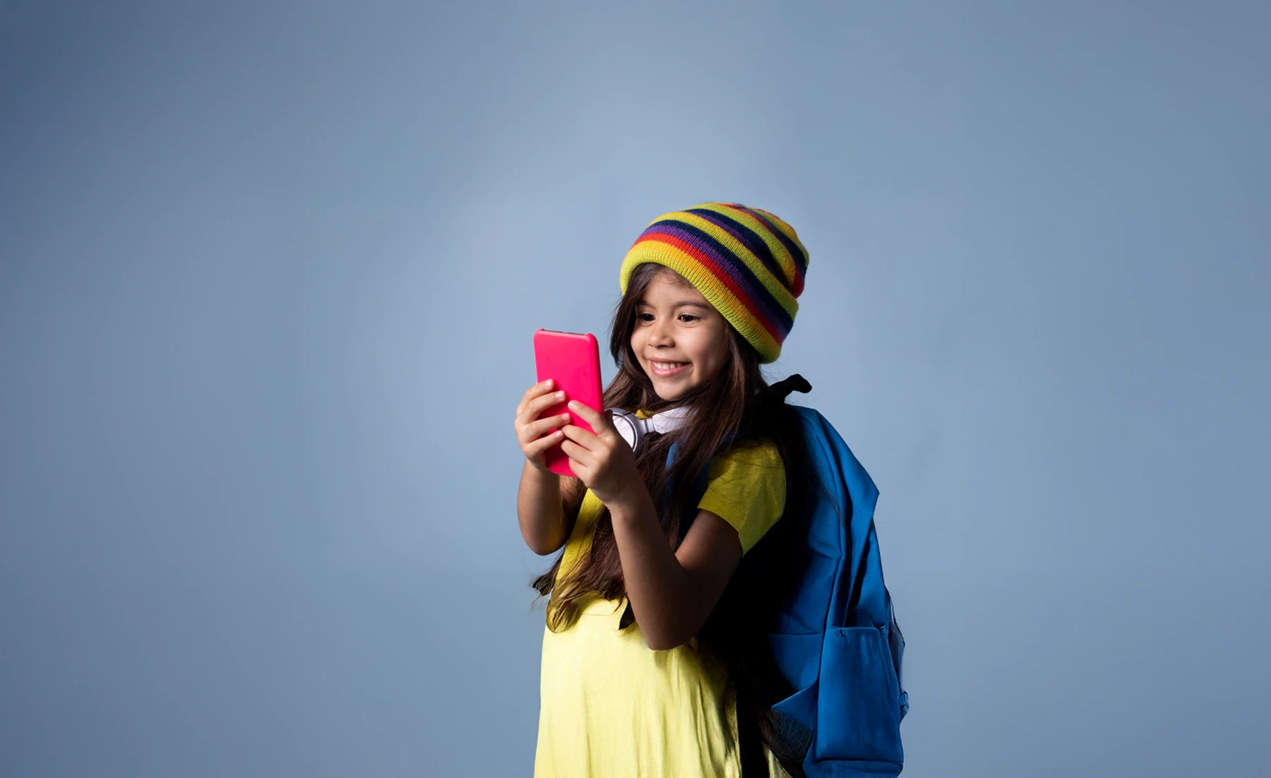Smiling girl in colorful hat using smartphone