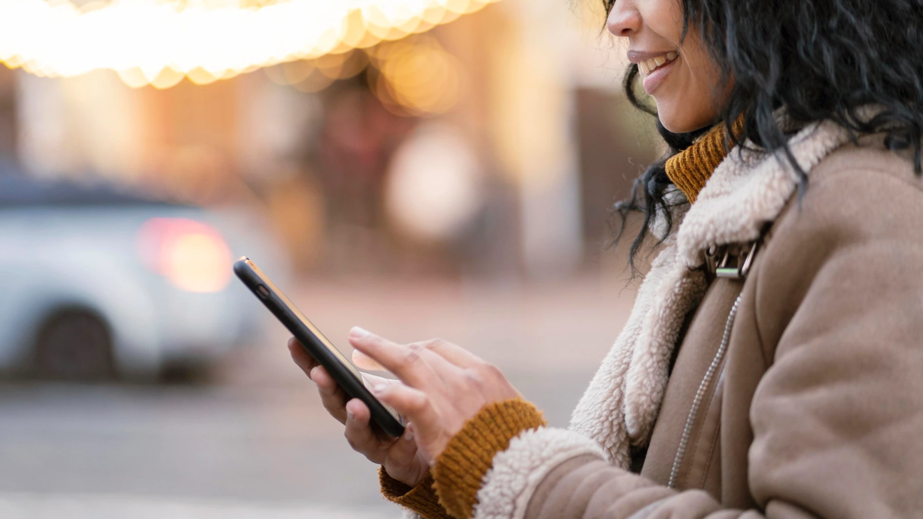 Person using smartphone outdoors with bokeh background.